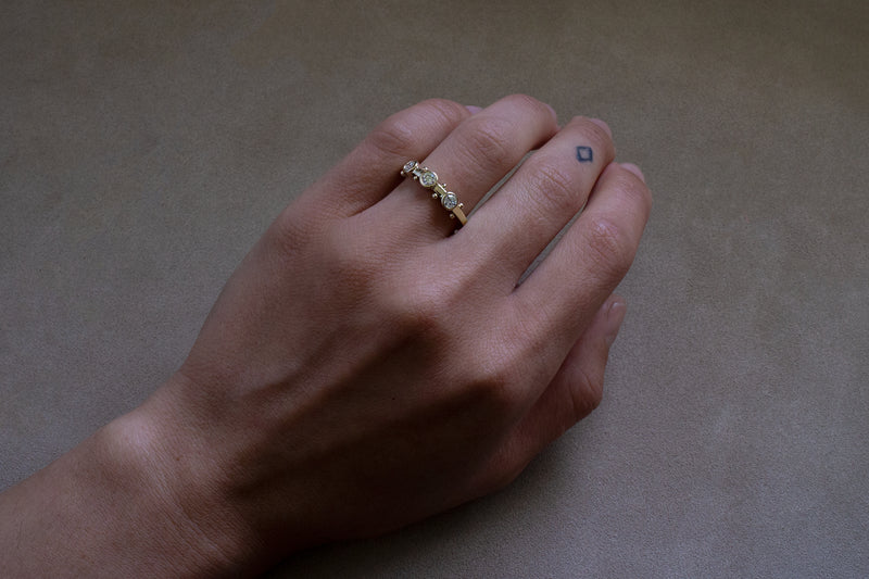 A hand wearing the Koemi ring on the ring finger against a tan background