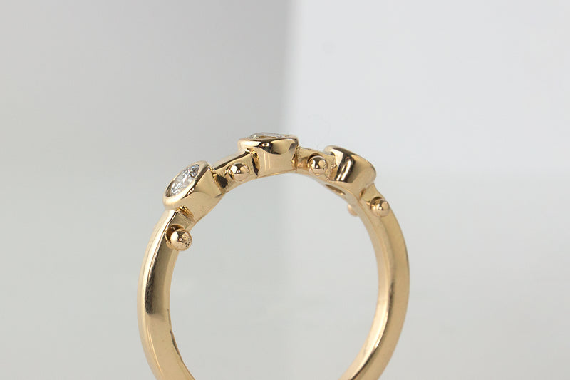 A closeup side view of yellow gold band with three small white diamond settings and two small yellow gold balls between each diamond setting along the sides of the band