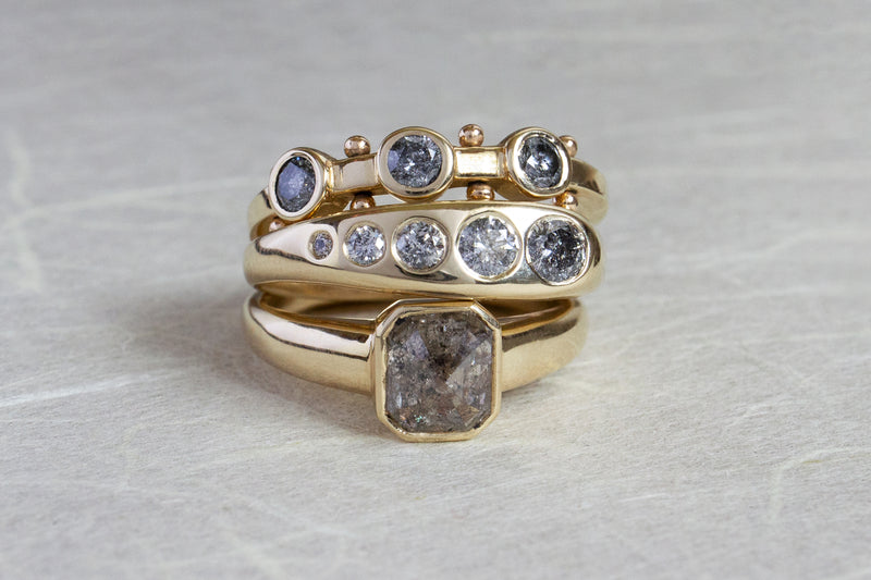 A stack of grey diamond yellow gold rings featuring the Koemi, Lila Sumprima and Takara rings 