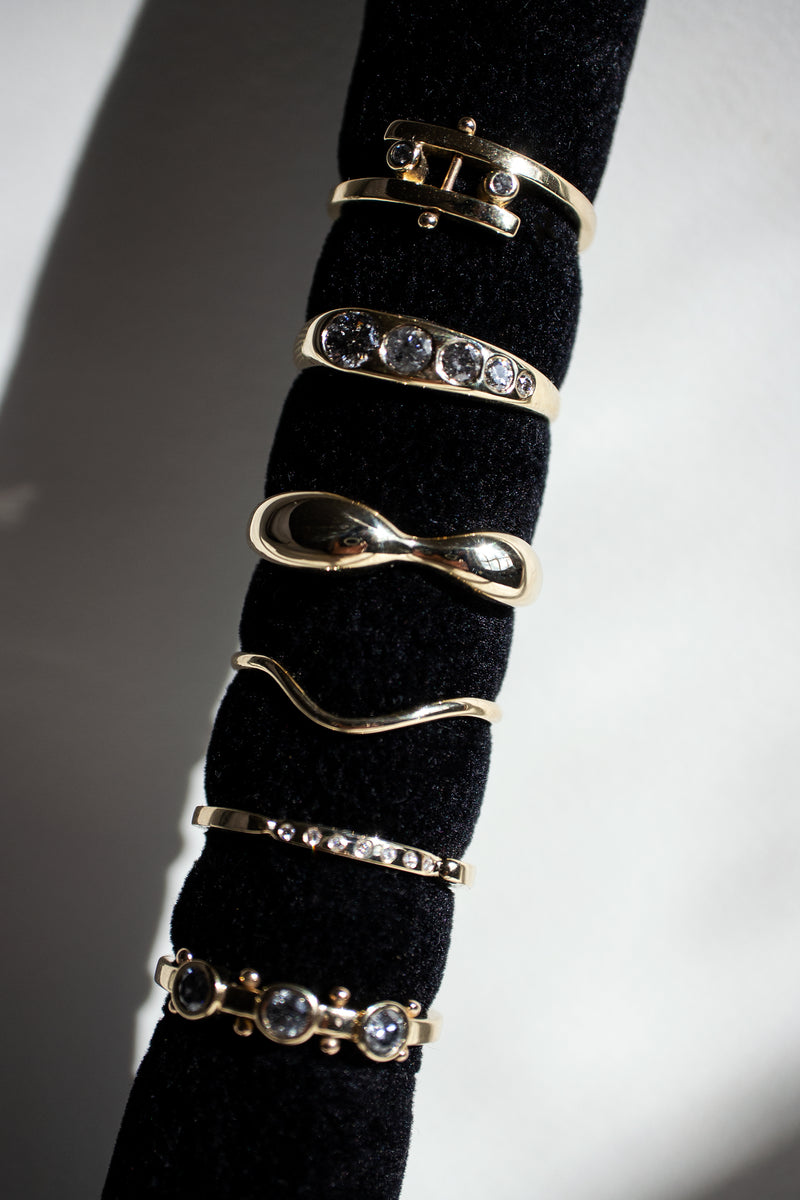 A roll of black velvet featuring the Kiyo, Lila Sumprima, Figure, Masumi Contour, Enzo, and Koemi yellow gold rings along it