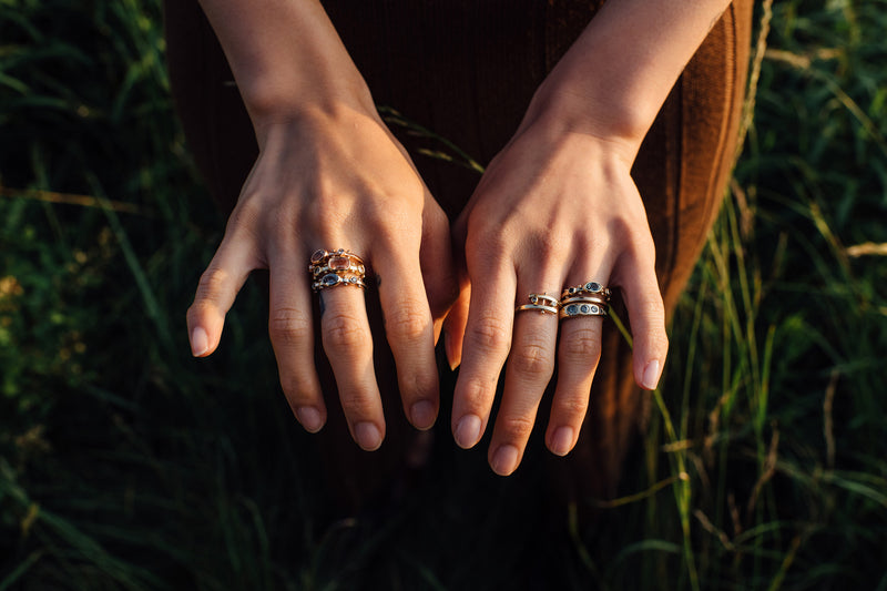 Two hands above a field of green grass with a styled stack of M.Hisae yellow gold rings