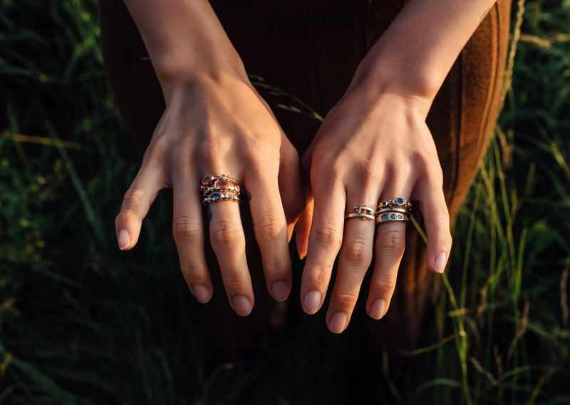 Two hands above a field of green grass with a styled stack of M.Hisae yellow gold rings
