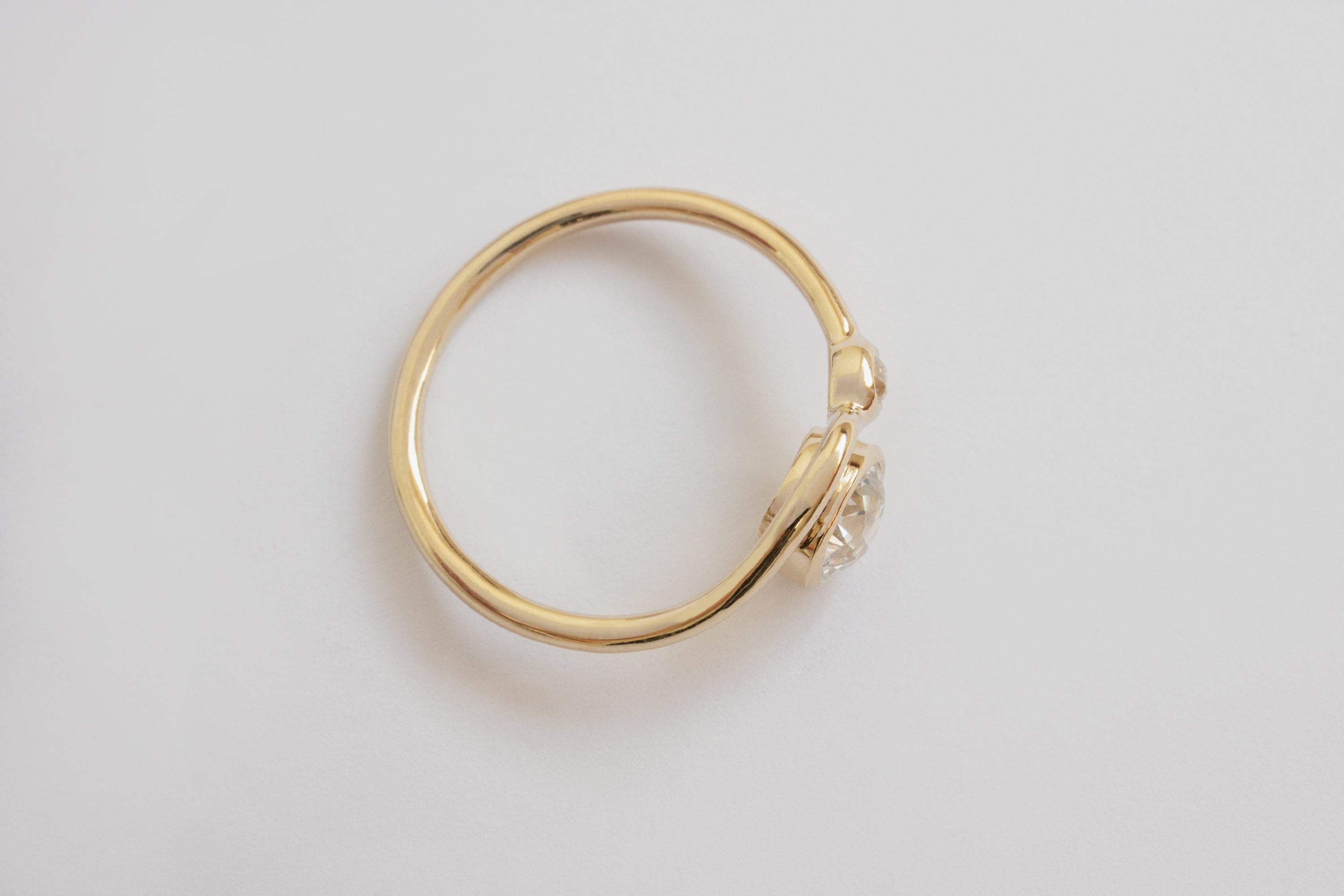 Top view of a bright white large round diamond and smaller diamond each framed in circular yellow gold setting on a wavy yellow gold band layered with another simple wavy yellow gold ring band