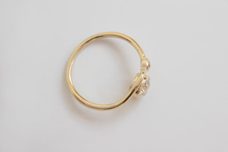 Top view of a bright white large round diamond and smaller diamond each framed in circular yellow gold setting on a wavy yellow gold band layered with another simple wavy yellow gold ring band