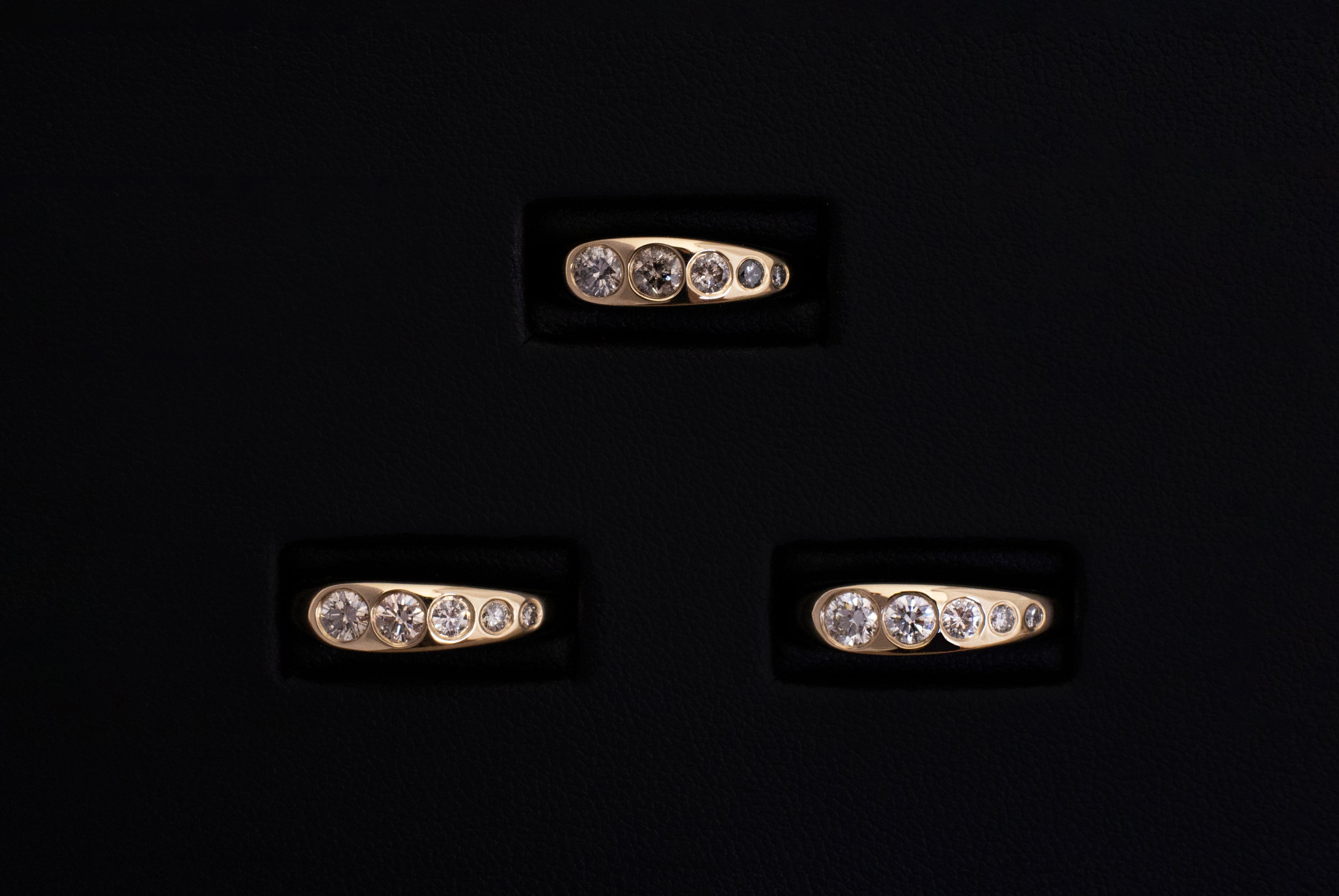 Three Lila Suprima Rings. Flush-set diamonds in a tapered gold band.